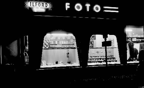 Skyltfönster kvällstid hos Fototjänst i Varberg, fotograf Märta Ågrens firma. Ett par av fönstren har en lätt konform. Hon hade butik och ateljé på Borgmästaregatan 1935-1962, och därefter etablerade hon butiken på Kyrkogatan i samma kvarter.