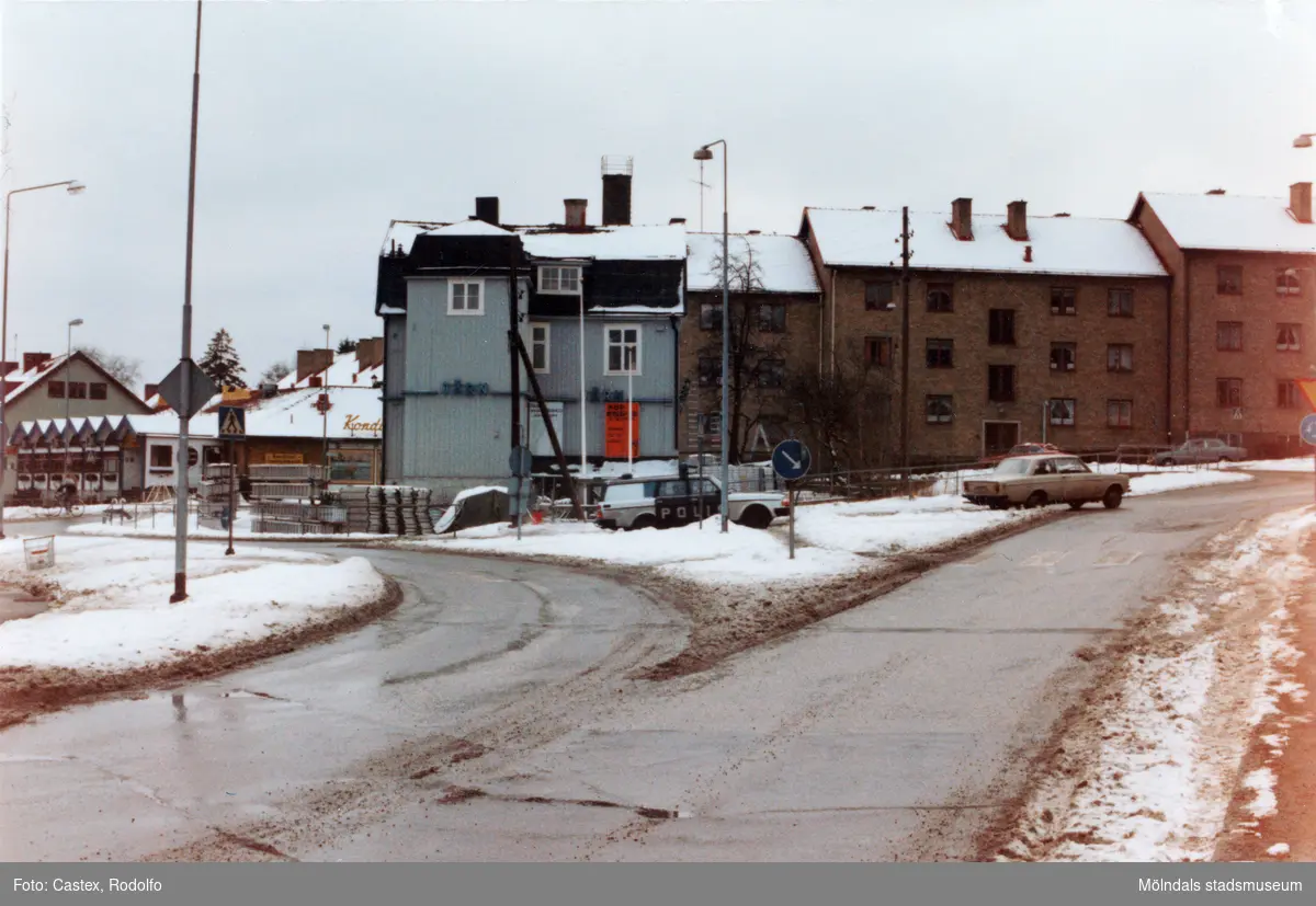 Trafik vid järnhandlarerondellen i Mölndals centrum i januari 1984. Joel Jacobsons järnhandel med adress Frölundagatan 30. I bakgrunden till vänster ses även Sahlins terrass.