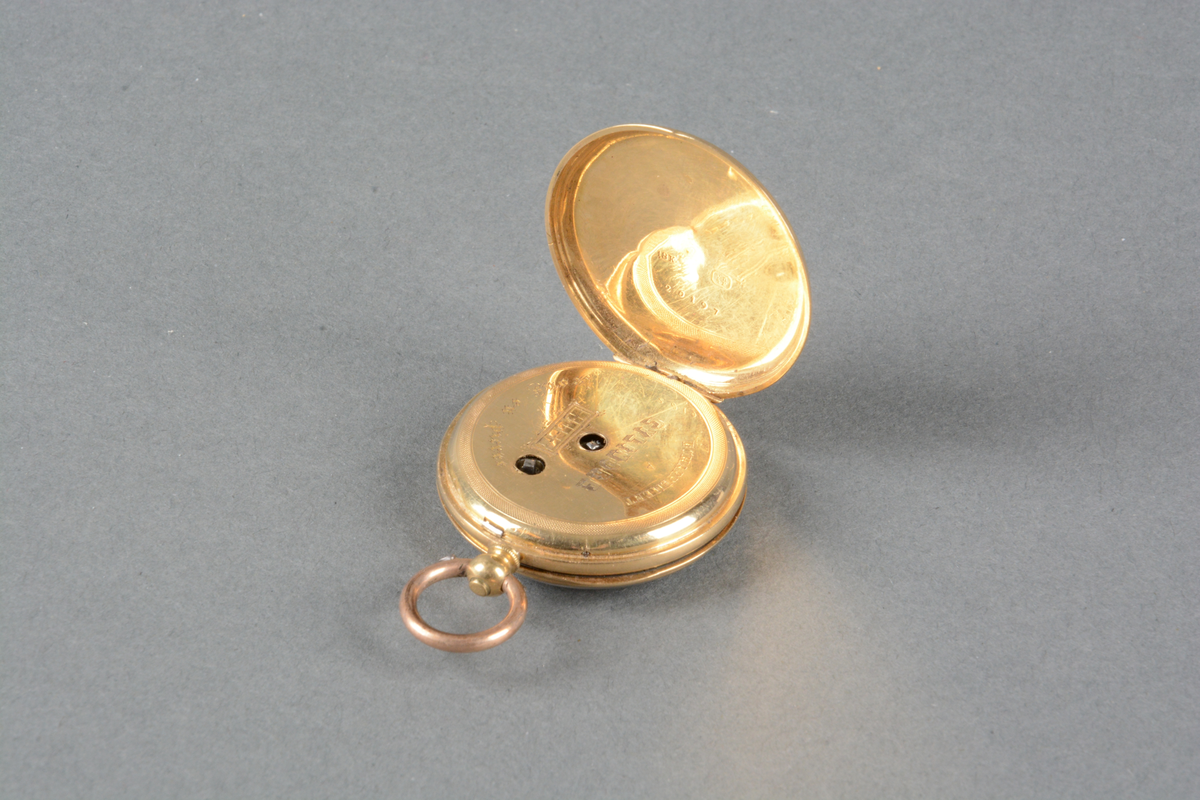 Dobbeltkapslet gull-ur. Hvit emaljeskive med sorte romertall, og spinkle gullvisere med liten dekordetalj på. Urets bakside er guillochert rundt et skjoldformet felt for initial (tomt). 
Det er ikke noe merke på skiven, men innerkapselen er merket med diverse skrifttyper: "ECHAPPEMENT A CYLINDRE trous en pierre" og i lokket 18K 20197
Merket i lokket: Theodor Olsen's Eftf. Juveler  Smaastrandgaten 4 Bergen.