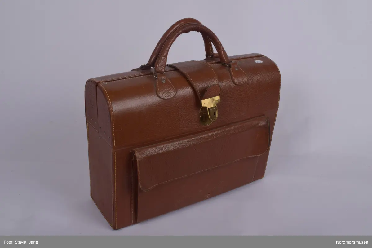 Legeveske i brukt skinn, åpning i toppen. Inneholder de fleste gjenstander man kan få bruk for ved sykebesøk. Dobbelt håndtak, lomme på utsiden kan lukkes med rein. Inni er hovedrom i bunnen med plastlommer med strikk øverst på en siden. Under denne to plastlommer med klaff. Et mindre skille av bunnen med skillevegg av gjenomsiktig plast. Inneholder numrene SU.3018a-3018s.
a) Etui for urinkatetere med fire katetre. Sylinder av gjennomsiktig plast med rød gummitopp i hver ende. 39 cm lang, 4 cm bred.
b) Sylindrisk metalletui i to deler for "smøreolje". Riller på siden fungerer som gjenger og dekorasjon. 78 cm langt, 4 cm diameter.
c) Todelt sylindrisk pappetui med reagensrør inni. 16,2 lang, røret 15,5 cm langt.
d) Termometer fra Villiers, merket ATOMIC. Liten glasshempe i toppen. 17 cm langt.
e) Tomt etui i messing med røde plastender. Irret.
f) Tomt etui i brunt skinn for blodtrykksapparat. Glidelås langs begges sider og topp. 17x12 cm.
g) Etui i eggehvit plast. Todelt med hengsling, inneholder staseslange produsert av Premeta Stauer. Brukes ved blodprøvetagning for å stramme rundt armen for å få fram blodårene.
m) Saks med krumme blader. 13 cm lang.
n) Skaplell med utfellbart blad. En skyvelås brukes for å hindre bladet i å folde seg sammen. Produsert av A. Rudds eftf. 14,5 cm lang utslått.
o) Anatomisk pinsett prdusert av Stille - Sverige. 13 cm langt.
p) To artieriepinsetter. Sakslignende pinsetter for å klipe igjen blodårer.
r) 4 pakker med steril suturtråd prod. av Davis & Beck Division American cyanid company. 1 pakke gasbind 4cmx5cm, 1 pk steril bomullsbandasje prod. av Beng & tegner & Co 25gr, 1 pk steril gasbind 1/4m, 1 stk trekantforkle 2,70.
s) 2 tungespatler i plast, 14,5 cm lang.