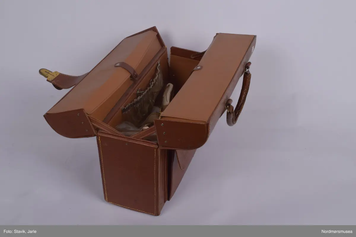 Legeveske i brukt skinn, åpning i toppen. Inneholder de fleste gjenstander man kan få bruk for ved sykebesøk. Dobbelt håndtak, lomme på utsiden kan lukkes med rein. Inni er hovedrom i bunnen med plastlommer med strikk øverst på en siden. Under denne to plastlommer med klaff. Et mindre skille av bunnen med skillevegg av gjenomsiktig plast. Inneholder numrene SU.3018a-3018s.
a) Etui for urinkatetere med fire katetre. Sylinder av gjennomsiktig plast med rød gummitopp i hver ende. 39 cm lang, 4 cm bred.
b) Sylindrisk metalletui i to deler for "smøreolje". Riller på siden fungerer som gjenger og dekorasjon. 78 cm langt, 4 cm diameter.
c) Todelt sylindrisk pappetui med reagensrør inni. 16,2 lang, røret 15,5 cm langt.
d) Termometer fra Villiers, merket ATOMIC. Liten glasshempe i toppen. 17 cm langt.
e) Tomt etui i messing med røde plastender. Irret.
f) Tomt etui i brunt skinn for blodtrykksapparat. Glidelås langs begges sider og topp. 17x12 cm.
g) Etui i eggehvit plast. Todelt med hengsling, inneholder staseslange produsert av Premeta Stauer. Brukes ved blodprøvetagning for å stramme rundt armen for å få fram blodårene.
m) Saks med krumme blader. 13 cm lang.
n) Skaplell med utfellbart blad. En skyvelås brukes for å hindre bladet i å folde seg sammen. Produsert av A. Rudds eftf. 14,5 cm lang utslått.
o) Anatomisk pinsett prdusert av Stille - Sverige. 13 cm langt.
p) To artieriepinsetter. Sakslignende pinsetter for å klipe igjen blodårer.
r) 4 pakker med steril suturtråd prod. av Davis & Beck Division American cyanid company. 1 pakke gasbind 4cmx5cm, 1 pk steril bomullsbandasje prod. av Beng & tegner & Co 25gr, 1 pk steril gasbind 1/4m, 1 stk trekantforkle 2,70.
s) 2 tungespatler i plast, 14,5 cm lang.