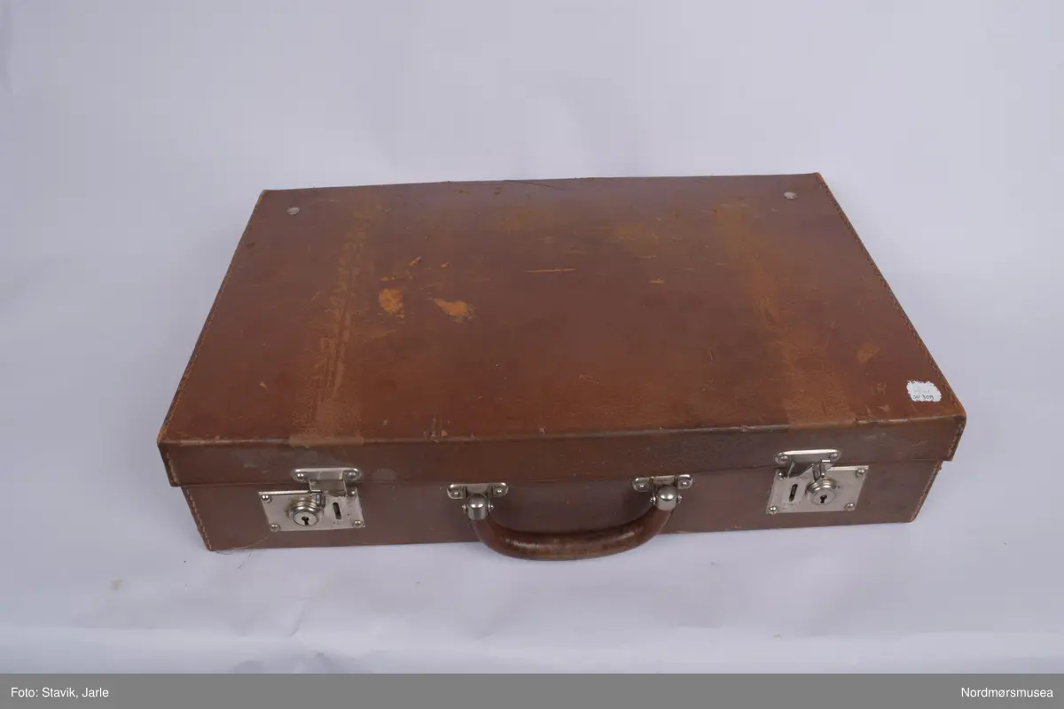 Koffert i brunt skinn.. Inneholder de fleste gjenstander man kan få bruk for ved fødsel. Full av utstyr a-å og aa-hh. Flere sylindre med diverse utstyr, noe løst utstyr, to tøyfuteraler for instrumenter.
a) Etui i rustfritt stål til børste merket Seifenbürste. Børsten i tre med krummet rygg. 10,5x3,7x3,4 cm. Børsten brukt til å skrubbe under neglene.
b) Etui til såpe i rustrfritt stål. Tomt, men lukter såpe. "Seife" på lokket. 8,2x4,2x2,5 cm.
c) Forniklet etui til oppbevaring av ampuller. Logo på lokket. Lokk hengslet, merket AESCULAP. 8x6,5x2,7 cm.
d) Sprøyte i forniklet etui med 2 spisser. "Original record" skrevet på lokket. 8x4x2 cm
e)Sylinderetui med lokk i begge ender. Hull i sidene på lokk og sylinder for lufting. 20,5 cm lang 7 cm diameter.
f) Sylinderlignende todelt sak. Ukjent funksjon. 8,3 cm diameter. 5,4 cm høyde.
g) 2 eterflasker 50g i brunt glass til bedøvelse oppbevart i kar i fødselskoffert.  "Eter til Narkose (Aether ad narcosin) N. sp. nr 2432. Tilsatt 0,001% DIEFENYLAMIN. Fabrikasjonsdatum 4. mar 1965." Prodsuert av A/S Den norske eterfabrikk. Målestreker med amrkering for 10.30 og 50 g.
h) Flat, rundt ekse i rustfritt stål.
i) Kar med utfoldbare føtter i rustrfitt stål til sterilisering med varmt vann.
j) Løslommer for obbevaring av instrumenter mm. Gult stivt tøy med solid skomakersøm.
m) Stort tøyfuteral i beige tøy med grå slitekanter. Trykknapper. Lommer og hemper inni med forskjellig fødselsutstyr. n-1 oppbevares i denne.
n) Simpsons fødselstang i rustfritt stål. I to deler for enkel sterilisering. Skeformede ender. Håndtaket har markerte fingergrept. Brukt til tangforløsning der fødselene får hjelp av en fødselstang i siste del av utdrivningsfasen. Dreier fosterhodet og trekker hodet gjennom fødselsåpningen. 35 cm lang.
p) Tang, arbortredskap i rustrfritt stål. Skarp saksaktig ende "til mutilering av foster i morsliv". Fjær på innsiden. Knapp for å holde tangen i stilling. Tangen er skap på utsiden i stedet for innsiden og spydformet når lukket. 27,5 lang, 4 cm langt blad.
q) Lang tang, sannsynligvis for "mutilering av foster i morsliv". Krummet ende, rillet på innsiden. Kan skrus sammen med skruer og vingemutter på enden. Kan deles i fire. 37 cm lang.
r) Pinsett, arteriepinsett til å klipe sammen blodårer med. 19,5 cm lang.
s) Nåleholder, sakslignede redskap for å holde suturnål. Haker for å låse den i stilling. 17 cm lang
t) Vaginalspekulum. Føres inn i skjeden for å holde den åpen under undersøkelser. Bøyd skaftende for bedre grep. Lik SU.3019u. 17cm lang,.
u)Vaginalspekulum ellers lik forrige bokstav.
v) Vaginalspekulum i rustfritt stål, føres inn i skjeden for å holde skjedeveggene åpne for undersøkelse. Fingergrept på skaftet med "avtrekker" til pekefinger for bedre grep. 22 cm lang.
w) Futeral i linstoff med tre trykknappet. Innvendig oppbevart forrskjellige instrumenter x-hh
x) Tang, kuletang, sakslignende instrument som brukes ved innsetting av spiral og gynekologiske undersøkelser. Rustfritt stål. 15 cm lang.
y) Lang kuletang, ellers lik x. 25 cm lang
z) Kuletang, lik y
æ) Korntang i rustfritt stål, rett skaft med mulighet for å låse den i sammenknepet stilling. 12,5 cm lang.
ø) Korntang lik æ
å) Sformet kateter (stikkes inn i urinøret for å tappe urin). Rustfritt stål.
aa) Spesialnål med mandreng. Mandreng er en nål som settes inn i hult rør eller kateter for at den lettere skal føres inn i organet som skal behandles. 9,5 cm lang.
bb) Spesialnål med mandreng 8 cm lang.
cc) Krum korntang i rustfritt stål, sakslignende med krummet ende. Kan låses i lukket stilling. 19 cm lang.
dd) Kirurgisaks med bøyd tipp i rustfritt stål. 14,5 cm lang.
ee) Korntang i rustfritt stål. Kan låses i lukket stilling.
ff) Tang, redskap for dilatasjon, utvide skjeden. Selvholdende slik at skjede forblir åpen. Håndtak rillet på hver ytterside av håndtaket. Mekanisme for å holde den åpen, justerbar. Krummet ende der tangendens bruksside er yttersiden. 16,5 cm lang.
hh) Rund eske i rustfritt stål til suturnåler. 3 nåler inni. Innskrift: AESCULAP. 6,5 cm diameter, 1 cm høy.
bb) 
