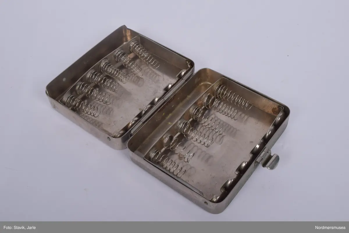 Legeveske i brukt skinn, åpning i toppen. Inneholder de fleste gjenstander man kan få bruk for ved sykebesøk. Dobbelt håndtak, lomme på utsiden kan lukkes med rein. Inni er hovedrom i bunnen med plastlommer med strikk øverst på en siden. Under denne to plastlommer med klaff. Et mindre skille av bunnen med skillevegg av gjenomsiktig plast. Inneholder numrene SU.3018a-3018s.
a) Etui for urinkatetere med fire katetre. Sylinder av gjennomsiktig plast med rød gummitopp i hver ende. 39 cm lang, 4 cm bred.
b) Sylindrisk metalletui i to deler for "smøreolje". Riller på siden fungerer som gjenger og dekorasjon. 78 cm langt, 4 cm diameter.
c) Todelt sylindrisk pappetui med reagensrør inni. 16,2 lang, røret 15,5 cm langt.
d) Termometer fra Villiers, merket ATOMIC. Liten glasshempe i toppen. 17 cm langt.
e) Tomt etui i messing med røde plastender. Irret.
f) Tomt etui i brunt skinn for blodtrykksapparat. Glidelås langs begges sider og topp. 17x12 cm.
g) Etui i eggehvit plast. Todelt med hengsling, inneholder staseslange produsert av Premeta Stauer. Brukes ved blodprøvetagning for å stramme rundt armen for å få fram blodårene.
m) Saks med krumme blader. 13 cm lang.
n) Skaplell med utfellbart blad. En skyvelås brukes for å hindre bladet i å folde seg sammen. Produsert av A. Rudds eftf. 14,5 cm lang utslått.
o) Anatomisk pinsett prdusert av Stille - Sverige. 13 cm langt.
p) To artieriepinsetter. Sakslignende pinsetter for å klipe igjen blodårer.
r) 4 pakker med steril suturtråd prod. av Davis & Beck Division American cyanid company. 1 pakke gasbind 4cmx5cm, 1 pk steril bomullsbandasje prod. av Beng & tegner & Co 25gr, 1 pk steril gasbind 1/4m, 1 stk trekantforkle 2,70.
s) 2 tungespatler i plast, 14,5 cm lang.