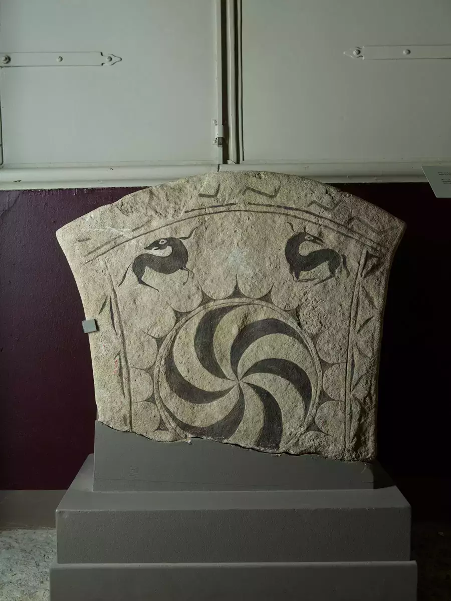 Påträffad i det romanska golvet i långhuset i samband med 1960-talets restaurering. Se sveriges kyrkor v:3 s. 331, fig. 394. Stenen finns upptagen som nr 64 i jan peder lamms katalog över bildstenar (nylén och lamm: bildstenar). Där uppges att stenen är kvar på fyndplatsen, ej återfunnen 1979. Obs utställd i bildstenshallen ! juli 2006/ml
av 400-talstyp. Dekorerad med solsymbol och bård, avbruten vid roten. Största höjd 58, största bredd 73, tjl. 11-15 cm.