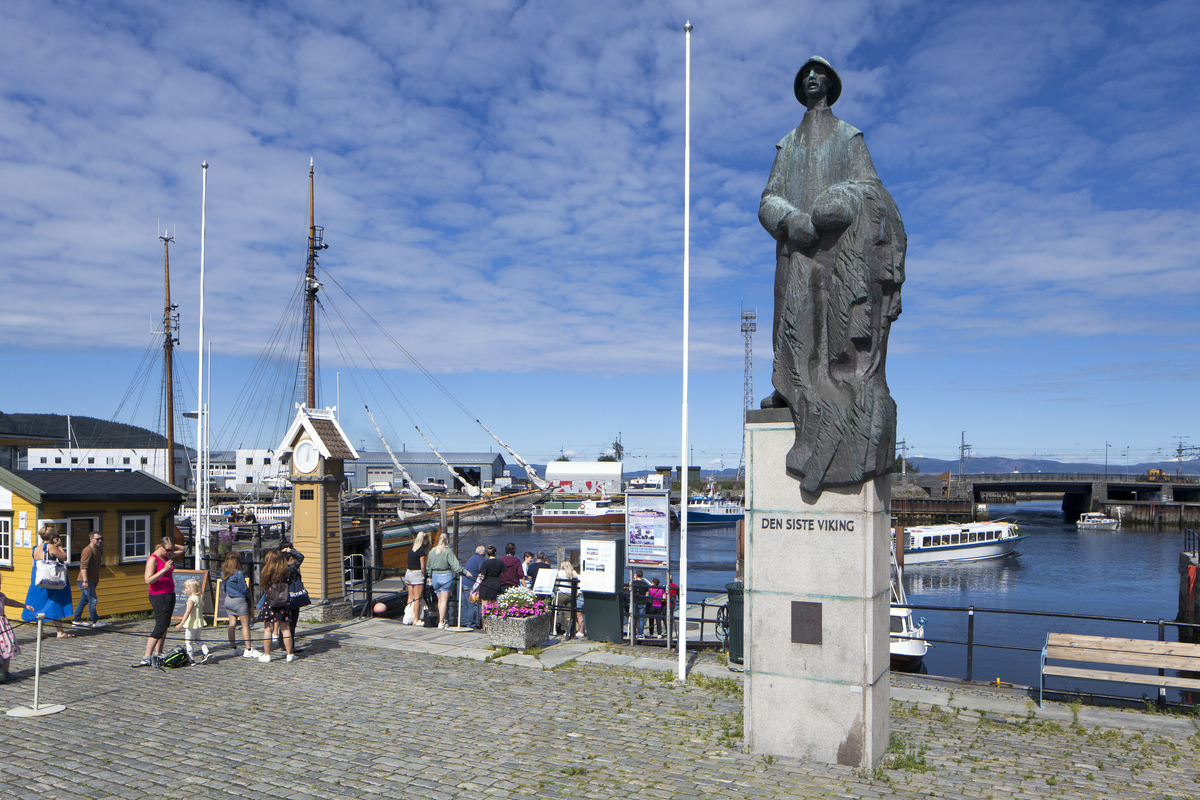 Helfigur på sokkel. En fisker som står med sitt fiskegarn i favnen. Antrukket i lang arbeidsfrakk og sydvest på hodet.