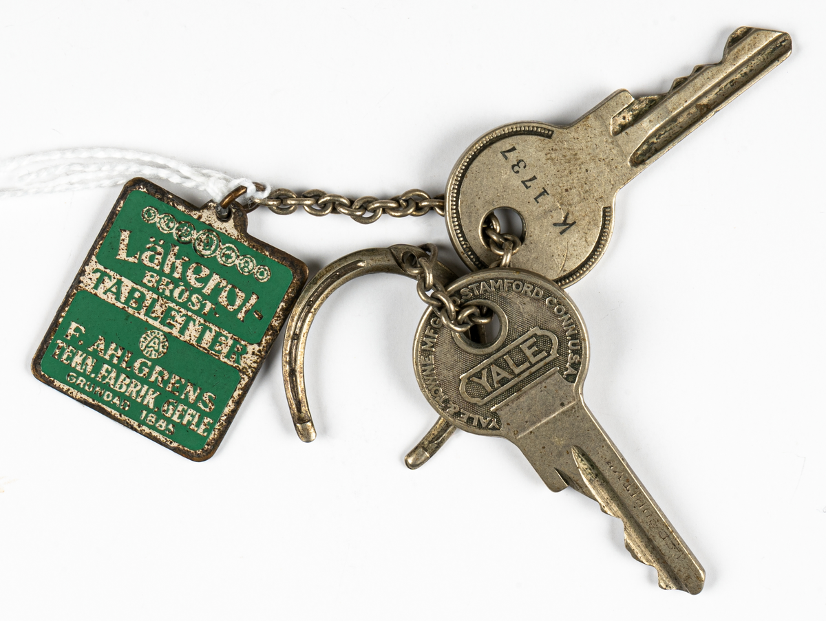 En nyckelring med två nycklar samt en hästsko med en nyckelbricka i metall, i form av en grön och vit Läkerolask. Nyckelringen hänger i en metallögla.