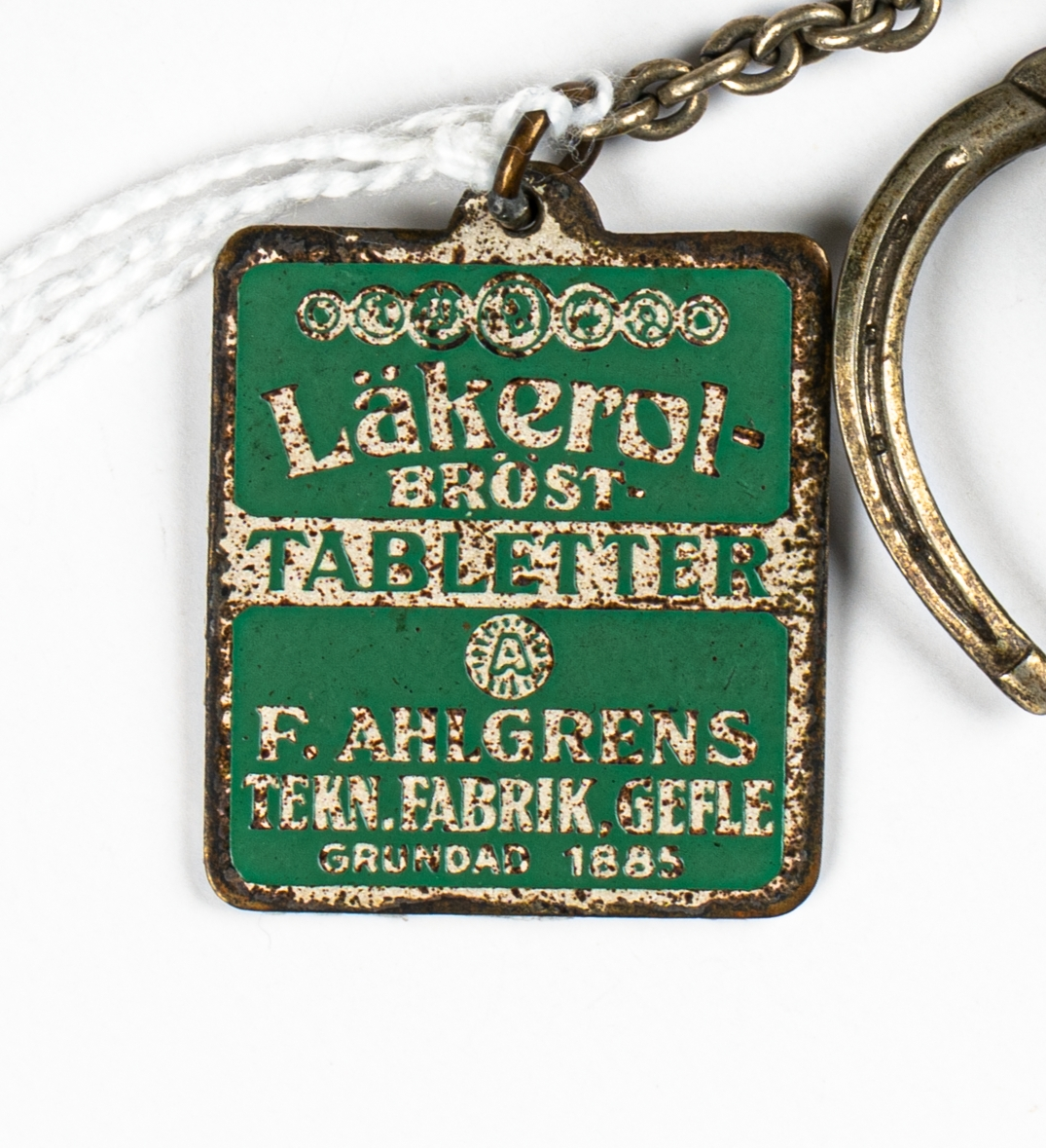 En nyckelring med två nycklar samt en hästsko med en nyckelbricka i metall, i form av en grön och vit Läkerolask. Nyckelringen hänger i en metallögla.