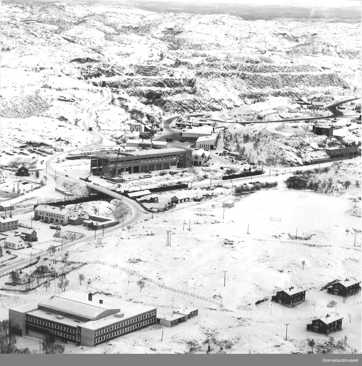 Bilde tatt fra luften av gruveselskapet A/S Sydvaranger sitt anlegg i Bjørnevatn, samt Bjørnevatn skole og lokal bebyggelse i nedre del av bildet.
