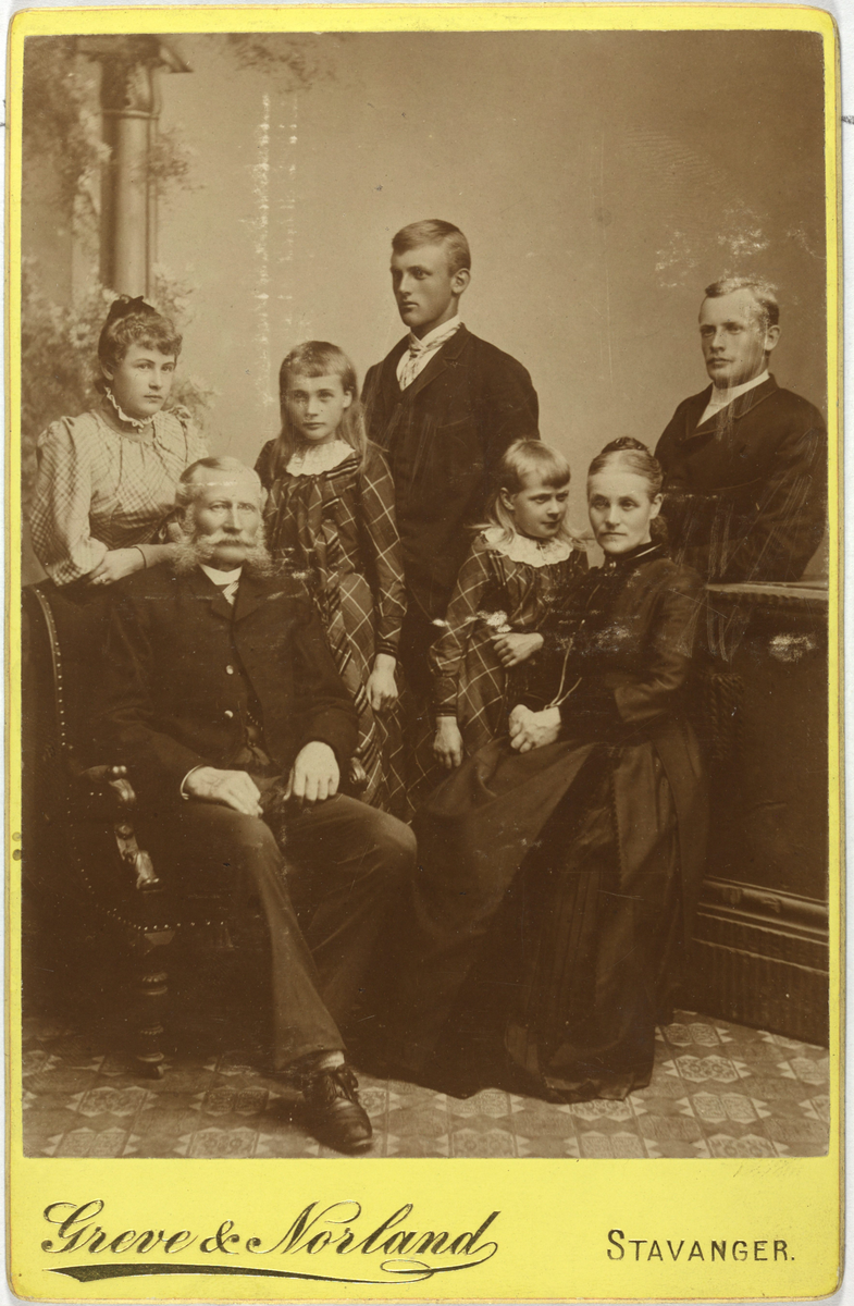 Atelierportrett, heilfigur av gruppe. Familiebilde, truleg ein bestefar, to foreldrar og fire barn.
