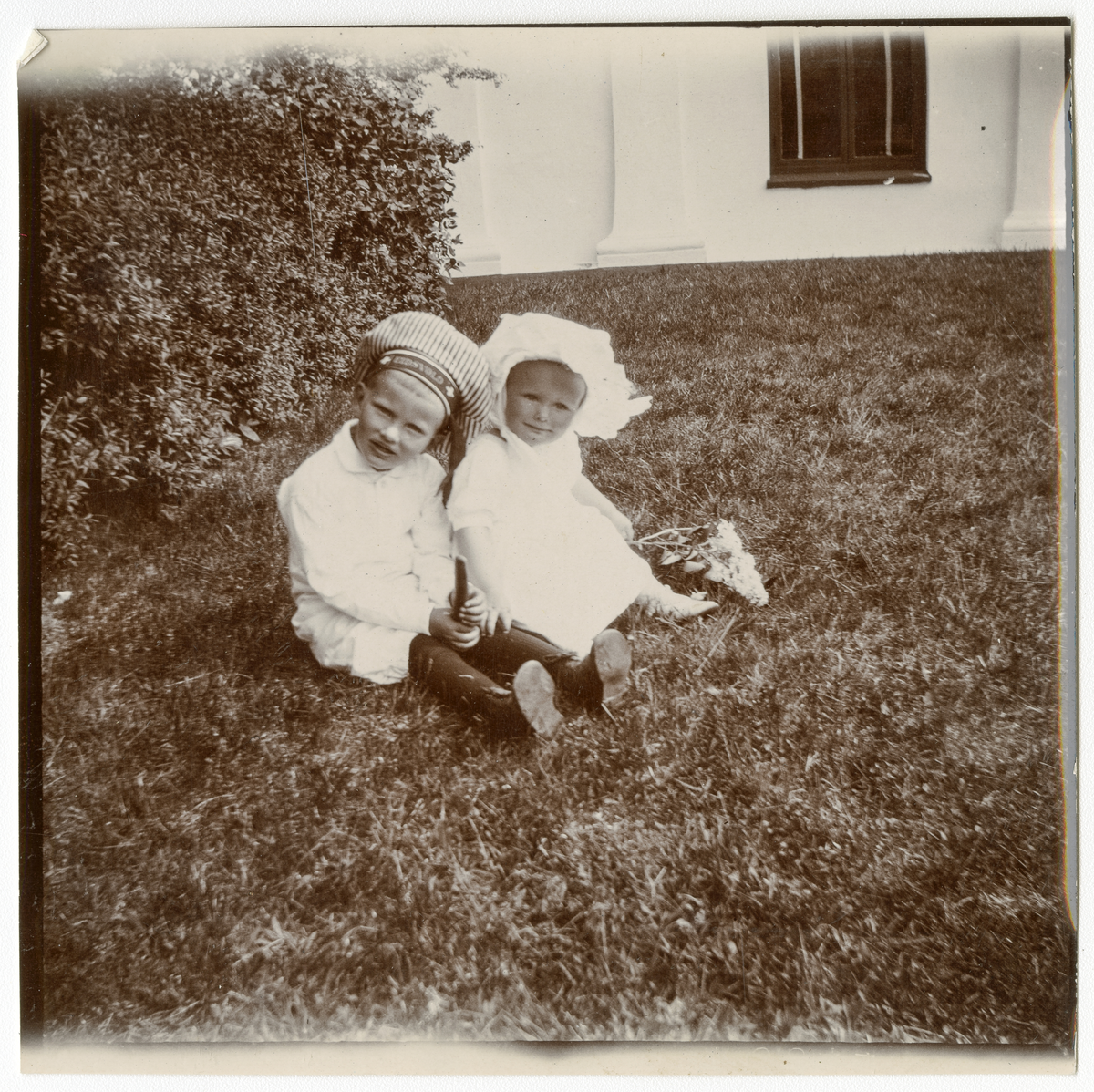 Foto av gutt og jente sittende i gress i 1915. Trolig søsknene Niels Frederik og Cecilie Aall