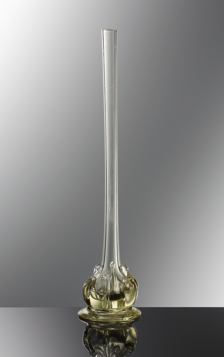 Gul orkidévas. Högt skaft som avslutas med en bottenkula. Kulan är överdraget med påklippt glas i organisk form.