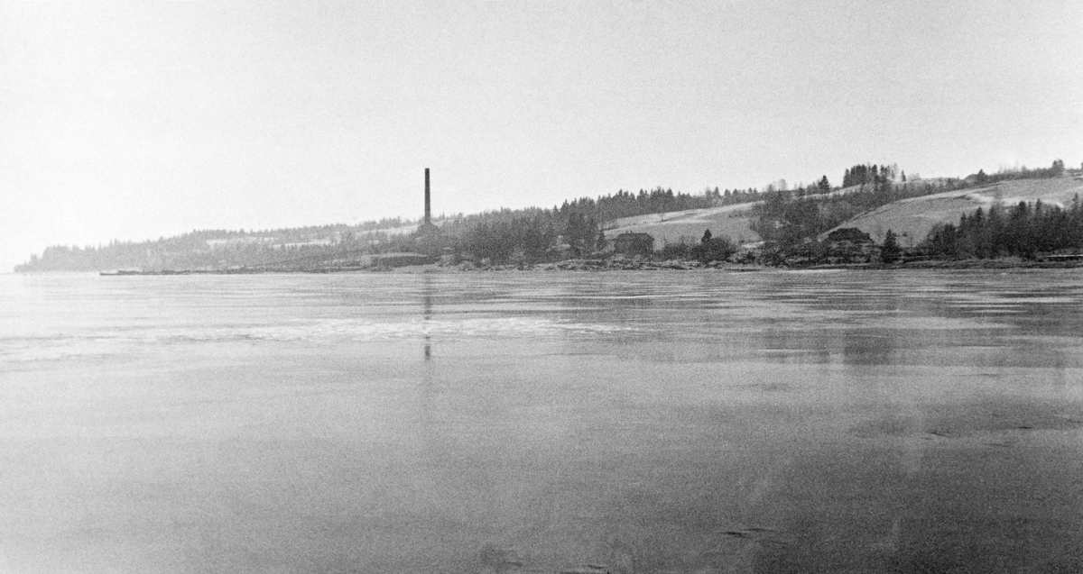 Her har fotografen forsøkt å dokumentere sprekker i isen på innsjøen Øyeren på Nedre Romerike. I bakgrunnen rager ei fabrikkpipe mot himmelen.