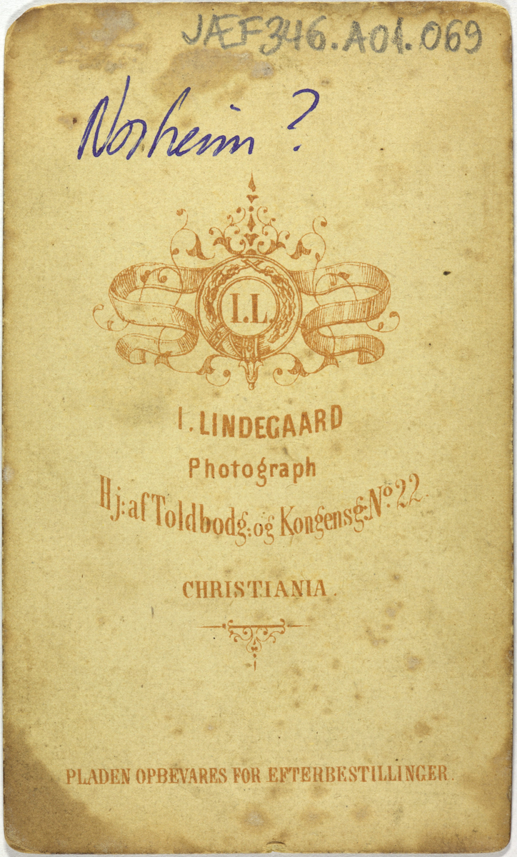 Atelierfoto av mann ved eit skrivebord. På baksida står det "Norheim?".