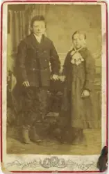 Atelierfoto av gut og jente, truleg søsken. Heilfigur, ståan