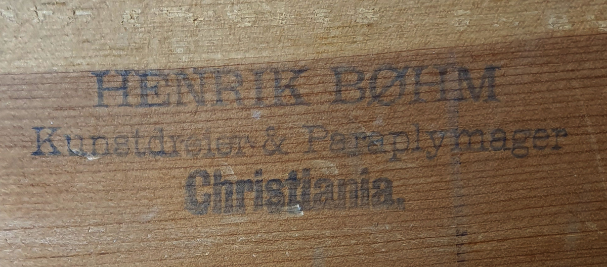 Rundt kniplingsbord av tre trukket med blå filt. En sylinderformet nålepute i midten. Til kniplingsbordet følger et trekk av bomullslerret som er brodert med blå initialer og har blå bånd langs kanten, som kan knytes rundt bordet.