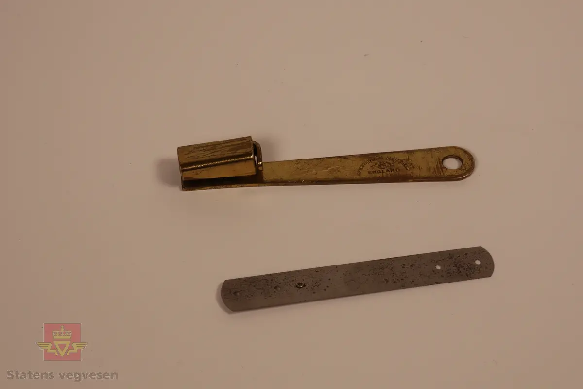 Verktøy til å reparere målebånd i metall i forskjellige bredder. inneholder skjøter i tre forskjellige bredder. 1cm, 1,3cm og 1,6cm. repareres ved å plassere en skjøt bak den knekte delen av et målebånd for å så nagle gjennom på hver side. Boksen er brun og åpnes ved å løfte av lokket. I  boksen finner man en tang for å feste nagler, metalskiver i tre størrelser til å repparere målebånd hvor noen er pakket inn i fettpapir. Det er også en liten grønn boks med en brun papirpose som inneholder nagler til tangen. 