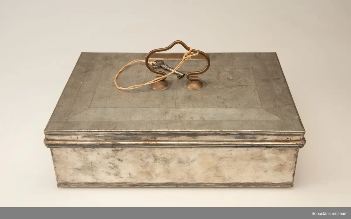 Rektangulär plåtlåda med lock. Handtag och nyckelhål. På lockets utsida en mässngsplåt med ingraverade texten GERTRUD ZACHAU.
Tillhörande nyckel.
Vid förvärvet innehöll skrinet fotogafier, se UMFA55947 och handlingar, se BMEA 488.