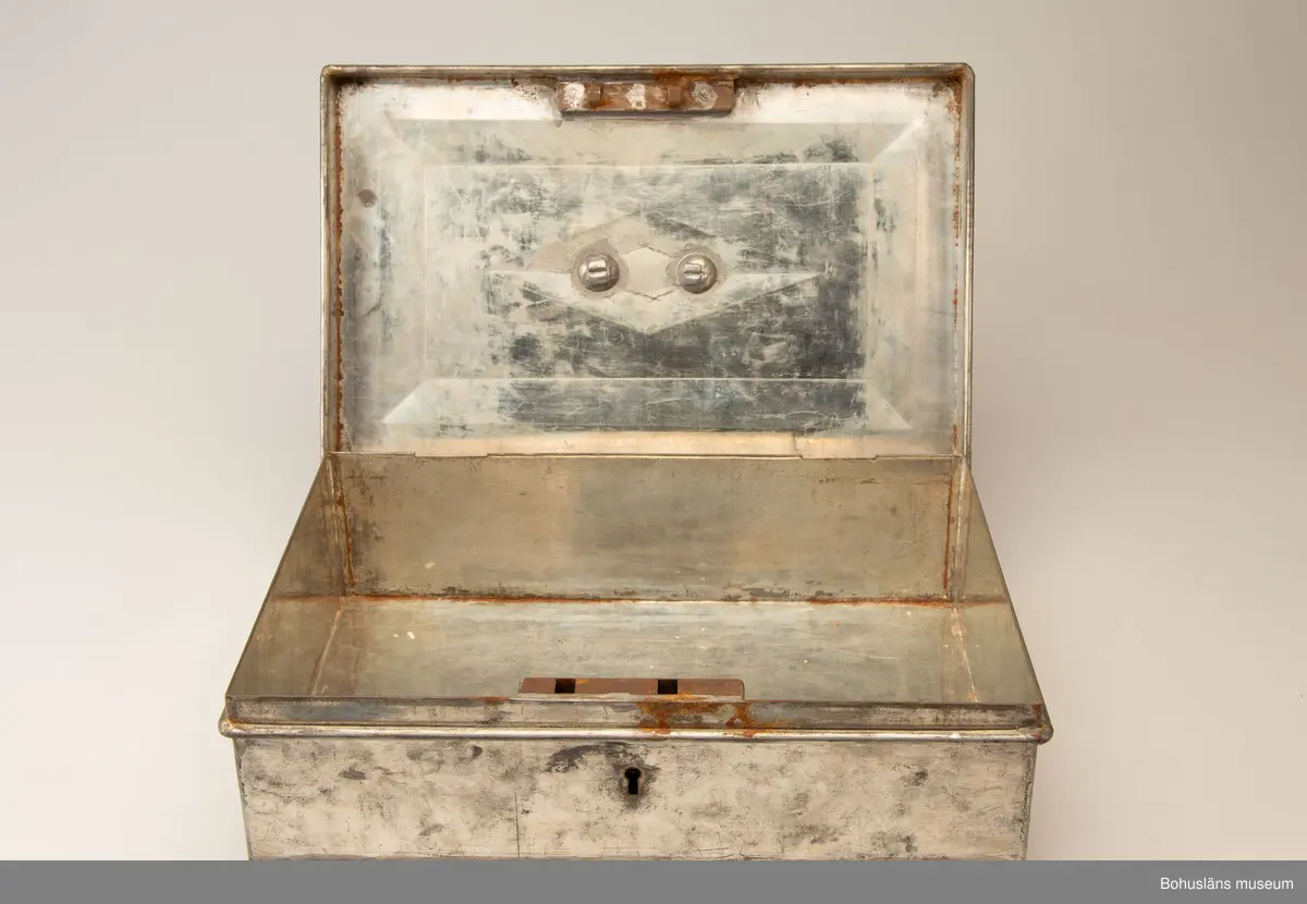 Rektangulär plåtlåda med lock. Handtag och nyckelhål. På lockets utsida en mässngsplåt med ingraverade texten GERTRUD ZACHAU.
Tillhörande nyckel.
Vid förvärvet innehöll skrinet fotogafier, se UMFA55947 och handlingar, se BMEA 488.