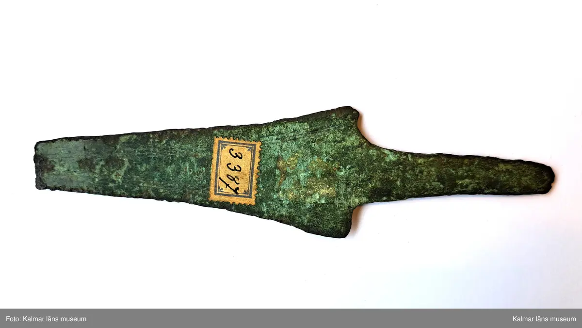 KLM 3387. Dolk, av brons. Med tvära skuldror och platt tånge. Klingan ornerad längs eggarna med tre enkla parallella fina linjer. Spetsen saknas.