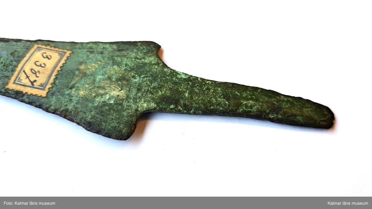 KLM 3387. Dolk, av brons. Med tvära skuldror och platt tånge. Klingan ornerad längs eggarna med tre enkla parallella fina linjer. Spetsen saknas.