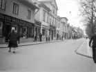 Ögonblicksbild från Storgatan i Linköping. 1929 var året och ännu en tid skulle gatans husrad spegla det föregående århundradet. Det närmaste huset, som vid tiden inrymde Bohlins guldsmedsaffär, kom att bli det enda hus som räddades när gatan senare breddades. Dock flyttades det ett tiotal meter söderut för att klara Storgatans nya bredd.