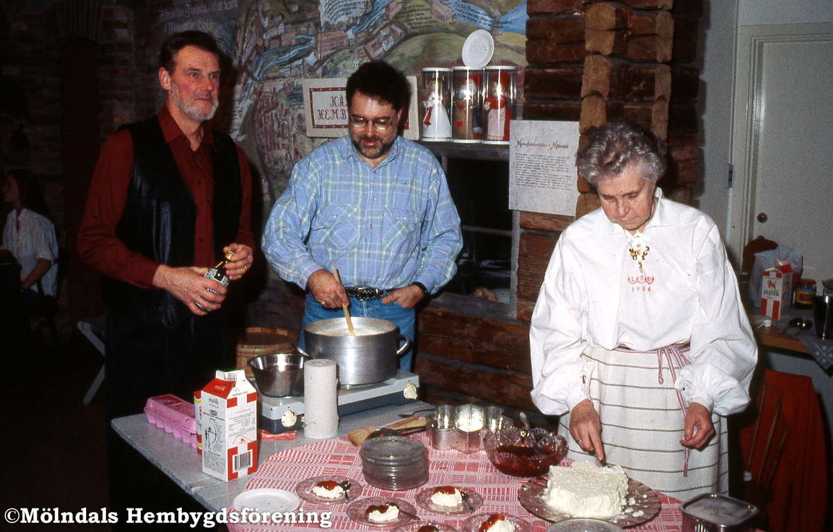 Kållereds Hembygdsgille serverar äggost på Mölndals museums julmarknad den 5/12 1993. Från vänster ses Berny Gustafsson, Staffan Bjerrhede och Lily Edvardsson som bär Kålleredsdräkten. Kv 16:21.