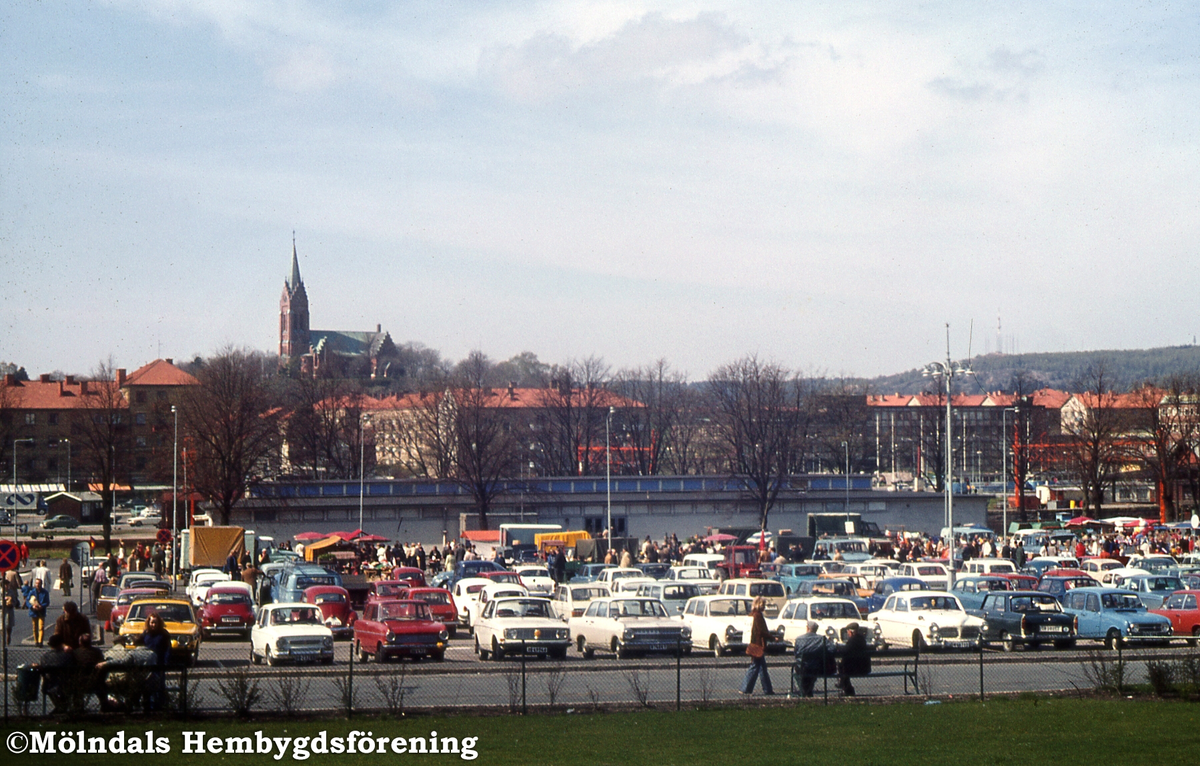 Nya torget i Trädgården, Mölndal, under en torgdag, år 1973. I torgets bortre del ses saluhallen och i bakgrunden ses bland annat Fässbergs kyrka.