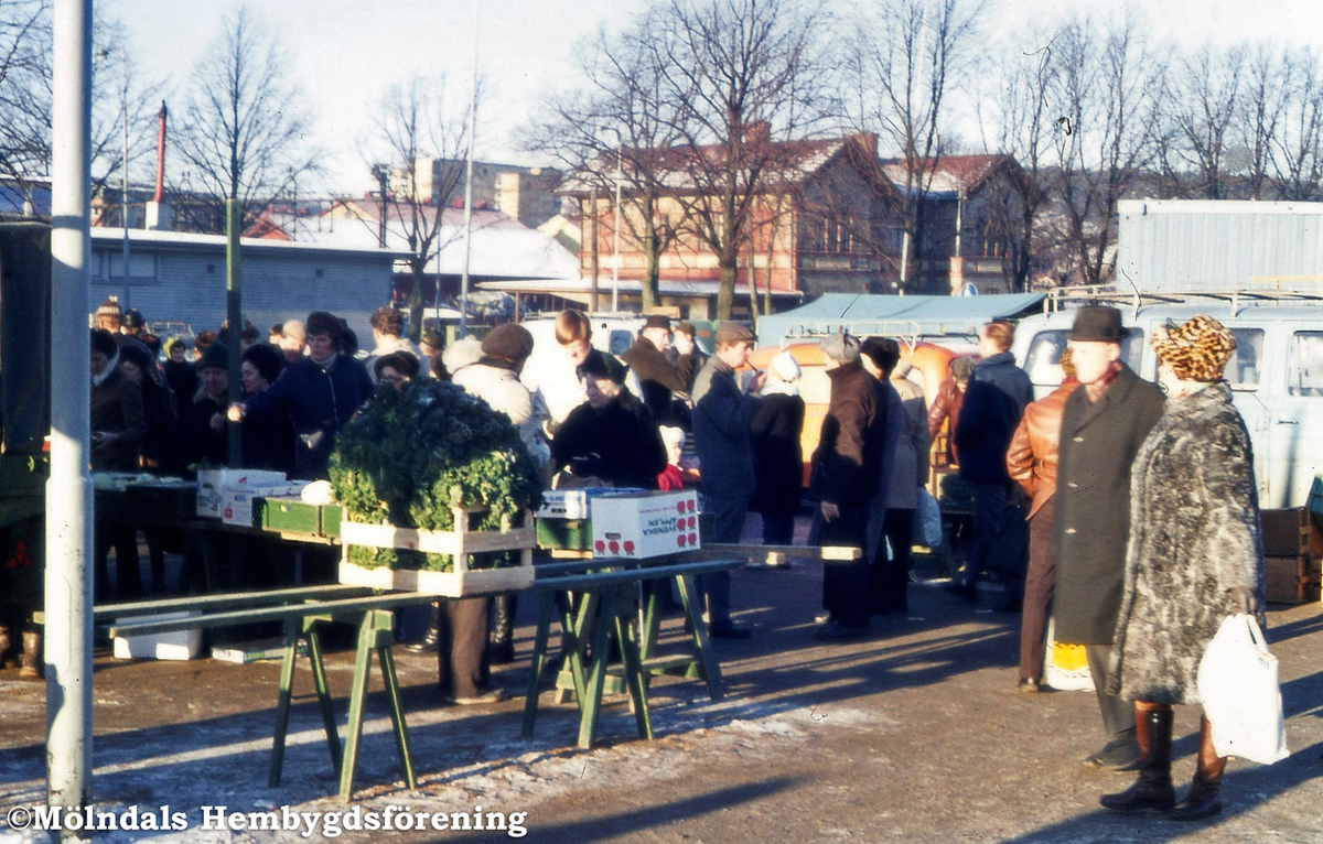 Torghandel vid Nya torget i Trädgården, Mölndal, år 1973. Personerna till höger är Sara och Helge Larsson. I bakgrunden ses även Mölndals Nedre järnvägsstation.