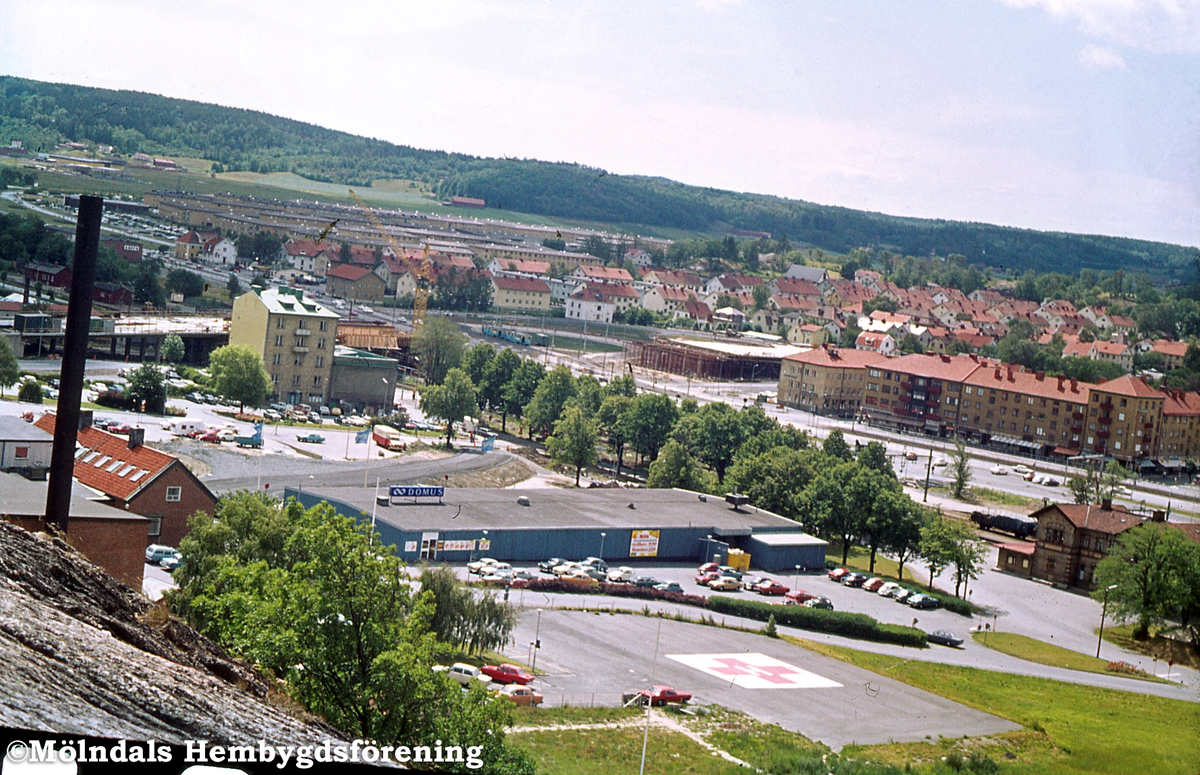 Nya torget i Trädgården, Mölndal, 1974-1975. Endast Domus blåmålade affärshall är kvar. Sista torgdag var 19 januari 1974. Veckan efter skedde torghandeln på Uddängen i Åby. Mölndals Bro är under uppförande.
