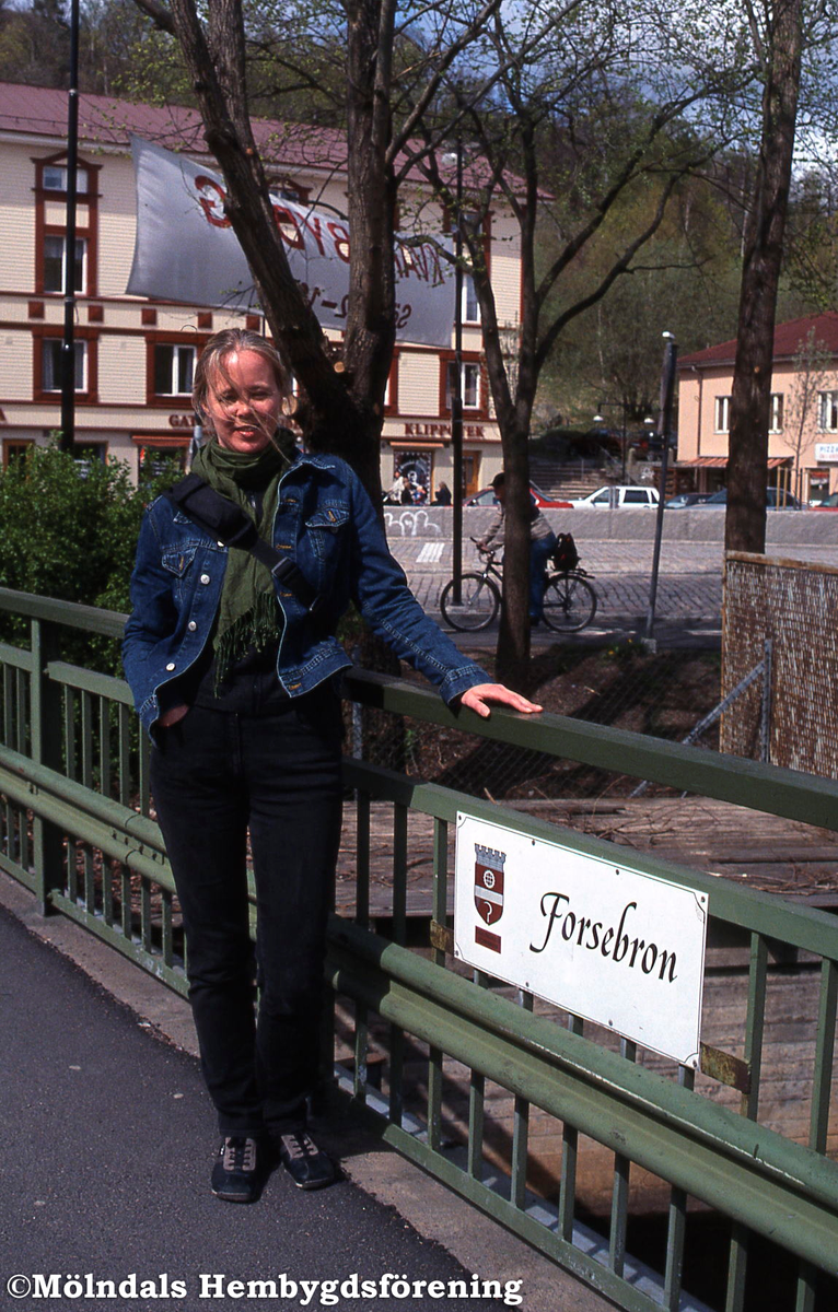 Vikarierande kommunantikvarie Anna Krus fotograferad på Forsebron i Mölndals Kvarnby under Kvarnbydagen den 28 april 2002. I bakgrunden skymtas bebyggelse vid Gamla Torget.