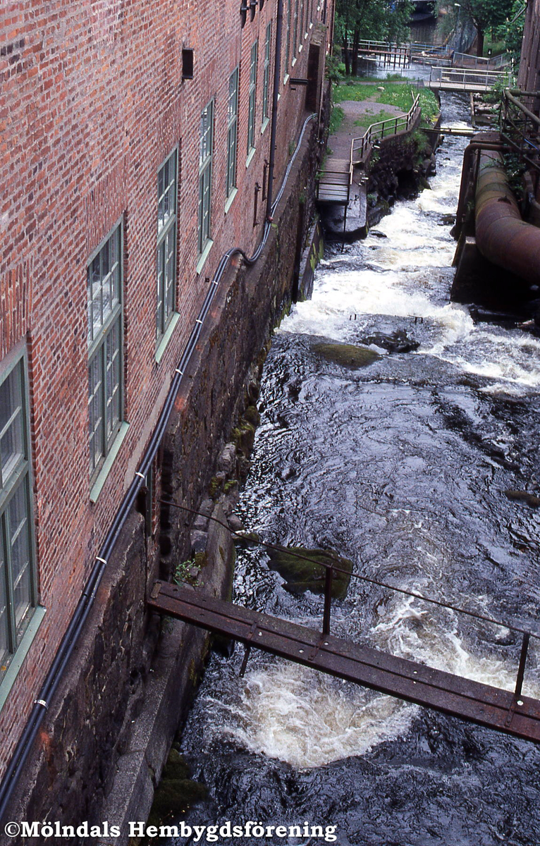 Fallet i Mölndals Kvarnby i höjd med industribyggnaden Stora Götafors, år 2002. Vy medtröms, ner mot Forsebron. På fasaden ses de hemska knippen av elledningar som satts upp utan tillstånd av fastighetsägaren Christer Harling. Energiverket fick ta bort dem.