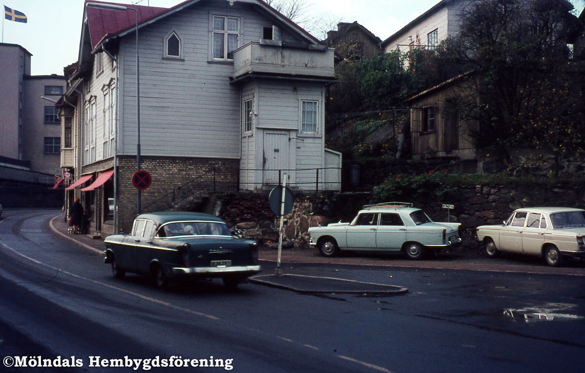 Trafik på Kvarnbygatan vid Gamla torget i Mölndal, 1970-tal. Huset närmast är Kvarnbygatan 37. I bakgrunden till vänster ses fabriksbyggnad tillhörande pappersbruket Papyrus.