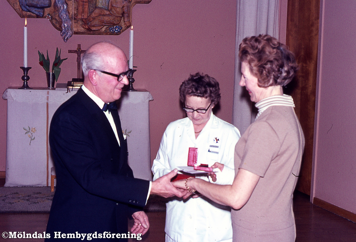 Lackarebäckshemmet i Lackarebäck, Mölndal, år 1969. Socialnämndsordförande John Svenning överlämnar guldklockor. Till vänster sjukskörska Astrid Lindström och tvättföreståndare Aina Kindlund.
