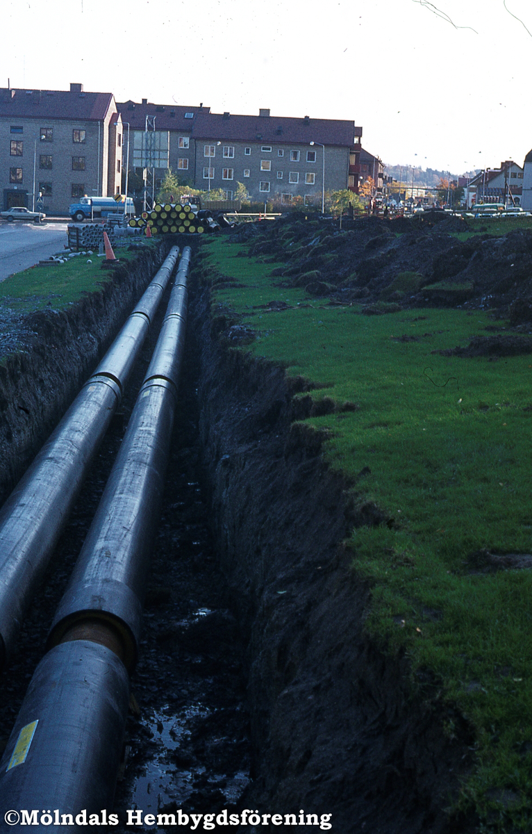 Fjärrvärme läggs utefter Häradsgatan i Bosgården, Mölndal, år 1982. Vy mot söder. I bakgrunden ses även bebyggelse vid Tempelgatan till vänster och till höger vid Storgatan.