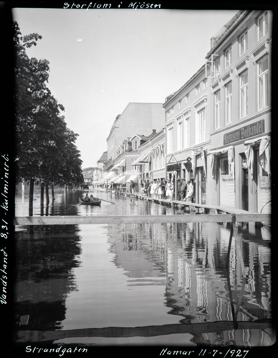 Hamar, Strandgata 13-15, Mjøsfommen 1927, barn i robåt, oppbygde gangbruer foran forrtningen til Magnussens Boghandel, 11. juli 1927 vannstand 8,31 meter, barna i robåten er Christian W. Lindmann og Hans Theodor Landstad,