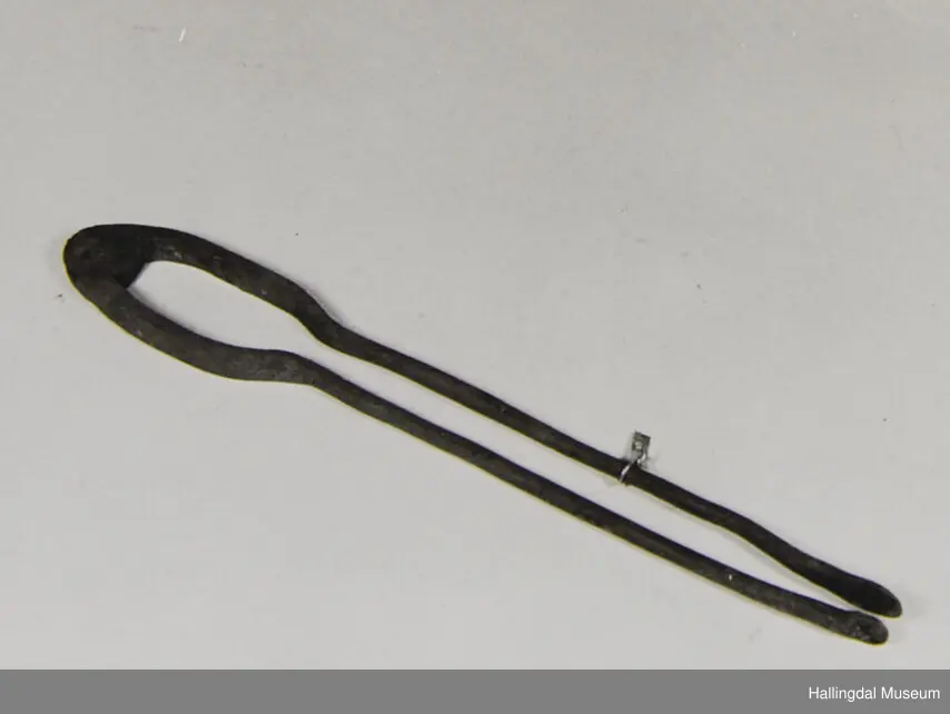 To jernstenger er hengslet sammen i endene. Innerst er de krumt fra hverandre. I den andre enden er de slått flate.