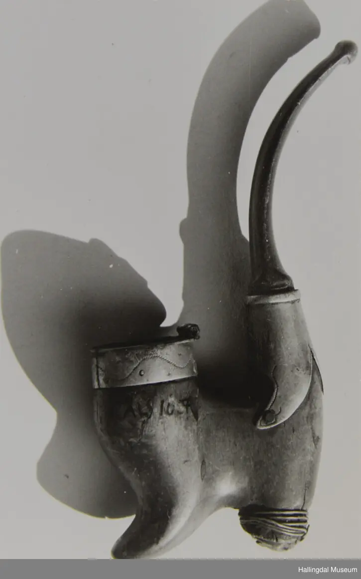 Munnstykket er av bein el. horn, lett bogeforma. Hovudet skore av bjørk. Sylvbeslag mellom hovudet og munnstykket og ytst på hovudet. Har vore lok på pipa.