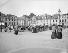Ögonblicksbild över Stora torget i Linköping. Dryga 100 år har passerat sedan bilden togs. Hästdragna kärror var ännu förhärskande och modet anständigt. I övrigt är miljön lätt igenkännlig för den som är förtrogen med staden. Större förändringar är tillkomsten av Carl Milles Folkungamonument och att husen rivits i kvarteret Apoteket bortom den tänkta skulpturen. Bild från omkring 1910.