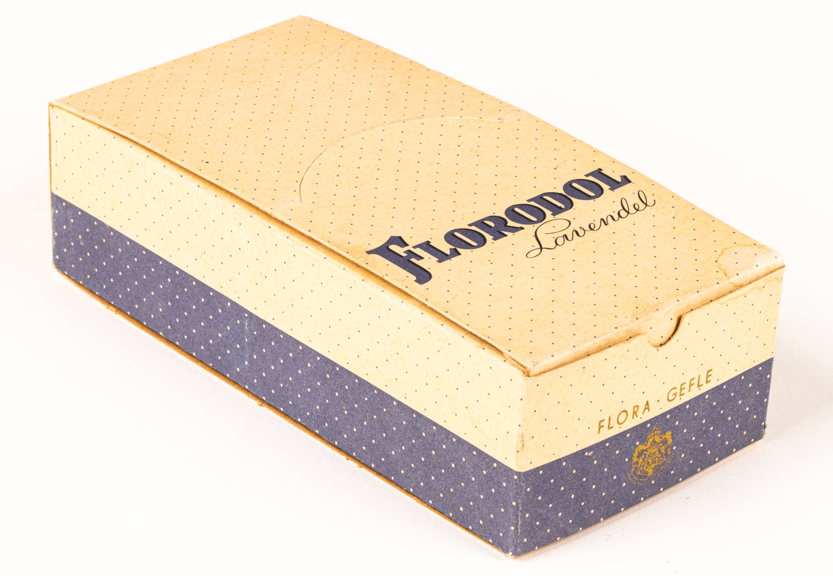 Tvålförpackning av papp. Rektangulär ask med tryck i grått på beige botten. Småprickig, grå fält på sidorna samt text: "Florodol Lavendel" och "FLORA GEFLE".