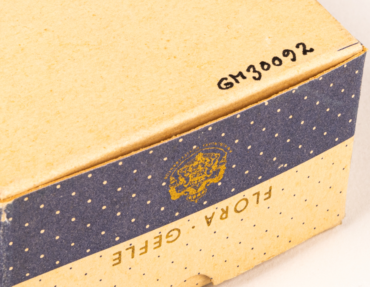 Tvålförpackning av papp. Rektangulär ask med tryck i grått på beige botten. Småprickig, grå fält på sidorna samt text: "Florodol Lavendel" och "FLORA GEFLE".