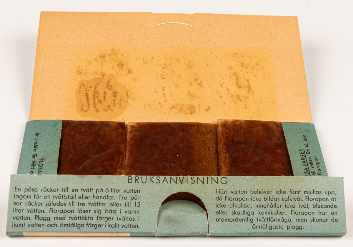 Tvättmedelsförpackning av papp. Obruten, innehåller tvättmedel. Platt, rektangulärt omslag. Tryck i blått, svart och rött på vit botten. På framsidan text: "Florapon fintvättmedlet" och "3 påsar - var och en för 5 liter vatten" samt "TEKN. A.B. FLORA GÄVLE" m.m. samt diverse klädesplagg. På baksidan finns "Dockan Flora", urklippsdocka med diverse kläder och medföljande hund "Fido".