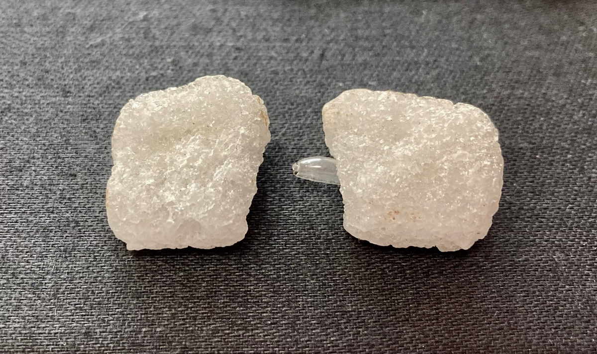 To sukkerbiter i glassylinder med metalllokk. Sylinderen er knust. Sukkerbitene inneholder svært små glassampuller.