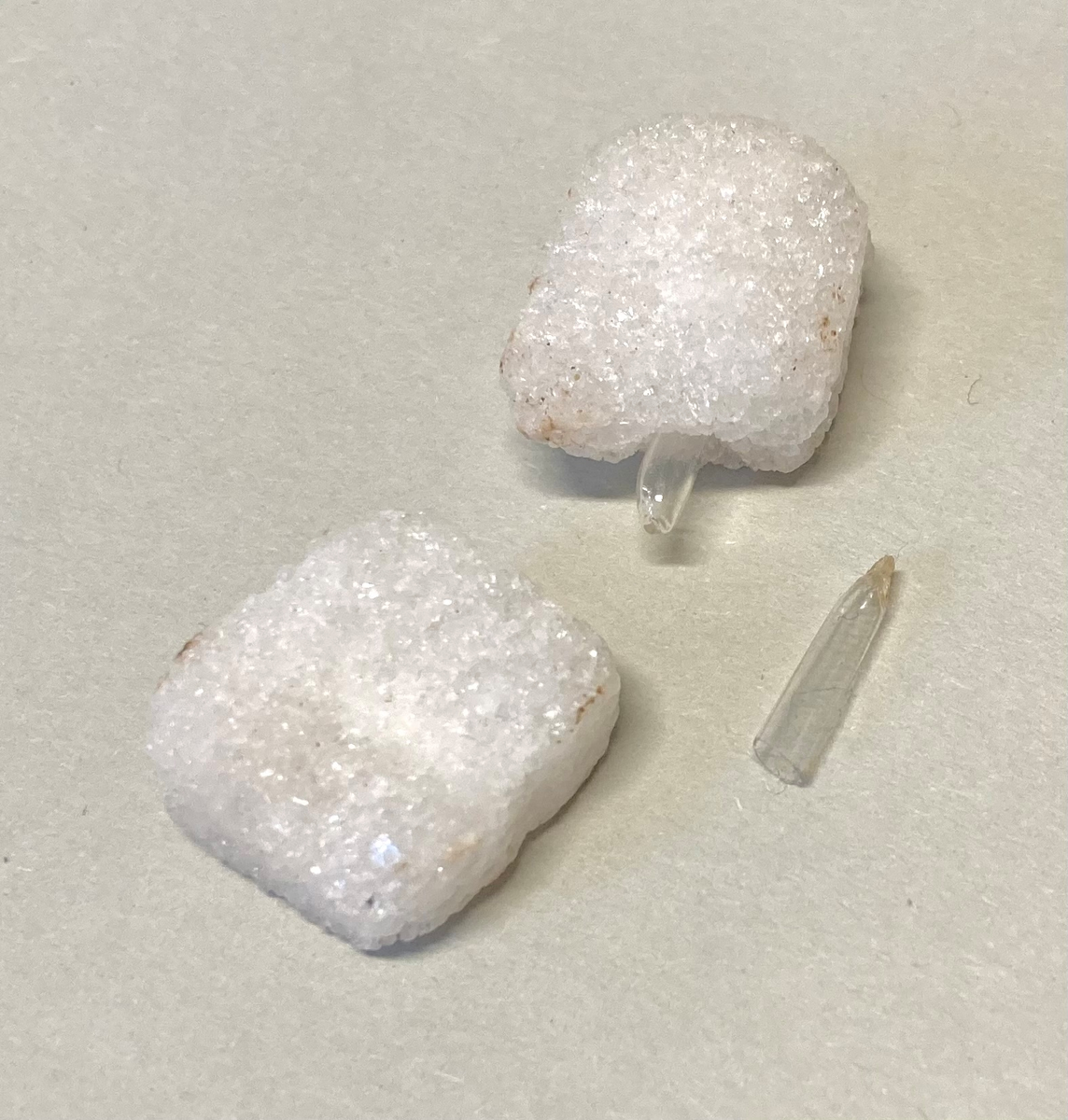 To sukkerbiter i glassylinder med metalllokk. Sylinderen er knust. Sukkerbitene inneholder svært små glassampuller.