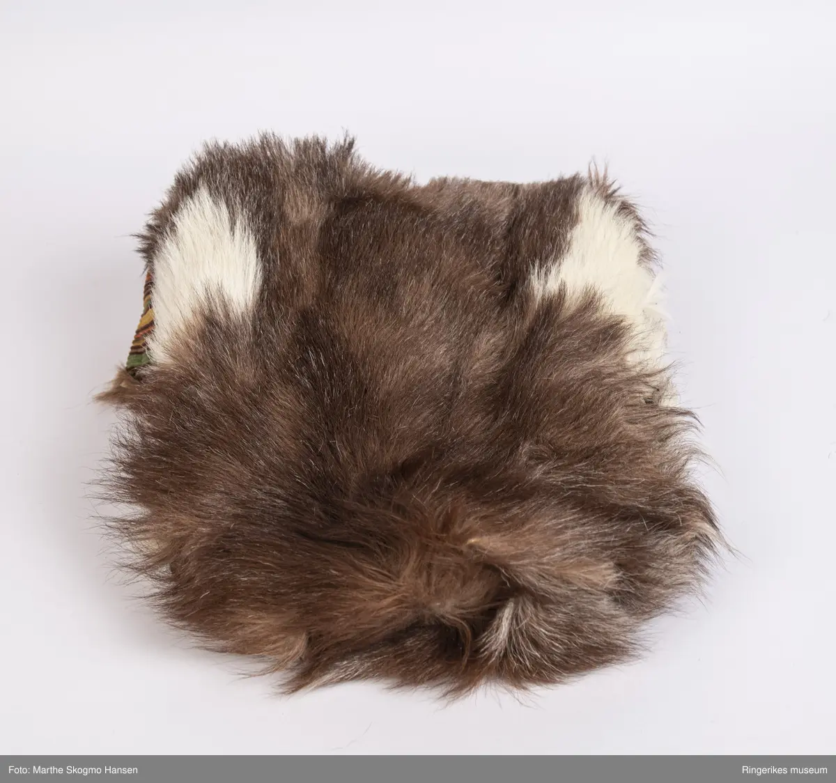 Sovepose til dokker. Posen er sydd av geiteskinn, som er brunt og hvitt. Innvendig er den foret med stripete cordfløyel. Posen ble sydd av Edel Gusgaard (1911-2000).