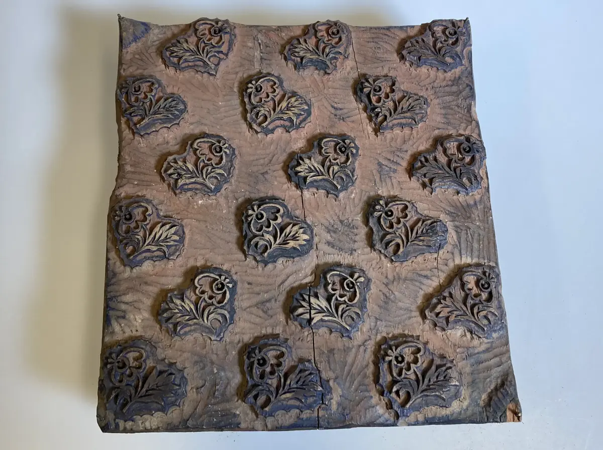 Av trä, med utskuret mönster föreställande spridda blommor och blad. På undersidan två halvmånformade urtagningar. Från Langska Kattuntryckeriet, Kopparsvik, Visby.
Avtryck finns bland Langs mönsterblad, inv.nr B288_2. Avtryck av detaljer på B288_1. Avtryck även i Langs receptbok som förvaras på Arkivcentrum Visby (Landsarkivet). En ritning med ungefär samma mönster finns bland Langs mönsterblad med inv.nr B288_71.
Påträffad utan inv.nr. Identifierad av fil.dr. Ingegerd Henschen-Ingvar, april 1964. Jämför A3205 och B1819. (från Langs verkstad).
