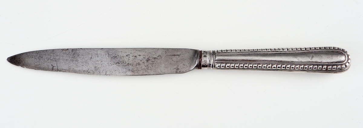 Kniv av silver.
Skaftet är tillverkat av pressat eller drivet silver, med dekor av pärlstavsbårder och längsgående räfflor. Stämplar (något svårtydda) på bladets infästning.

Inskrivet i huvudbok 1903.