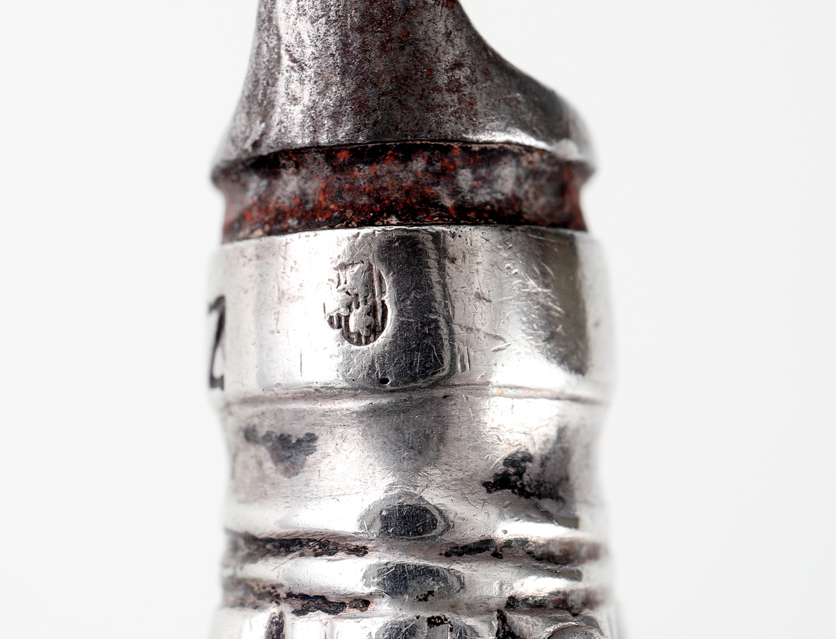 Kniv av silver.
Skaftet är tillverkat av pressat eller drivet silver, med dekor av pärlstavsbårder och längsgående räfflor. Stämplar (något svårtydda) på bladets infästning.

Inskrivet i huvudbok 1903.