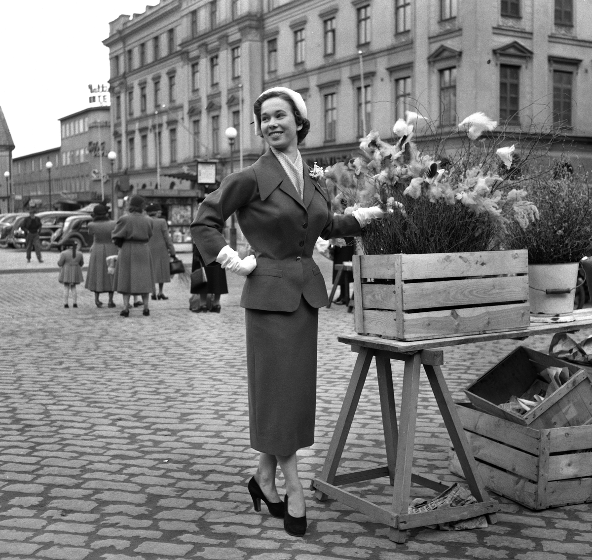 Inga Lill Lindblad visar upp ett plagg från linköpingsfirman Andersson & Beckman. Firman hade årliga modevisningar i Linköping. I slutet av mars år 1953 var det högsta modet tulpansiluetten, man kan se den typiska formen på det nedhasade axelpartiet på dräkten. Andersson och Beckman vid Stora torget i Linköping. Formella namnet på affären var AB Andersson, Beckman & co. Företaget grundades som diversehandel år 1852, senare koncentrerades verksamheten till manufakturaffär. Mode. Kläder. Påskris. Stora torget i Linköping. Handel. Påsk. 
...

385 bilder om Linköping på 1950-talet från tidningen Östgötens arkiv. Framtidstro och optimism är ord som sammanfattar Linköping på femtiotalet. Årtiondet innebar satsningar för att förbättra linköpingsbornas livsvillkor. Bostadsfrågan och trafiklösningarna dominerade den lokalpolitiska agendan.
Bilderna digitaliserades år 2013.