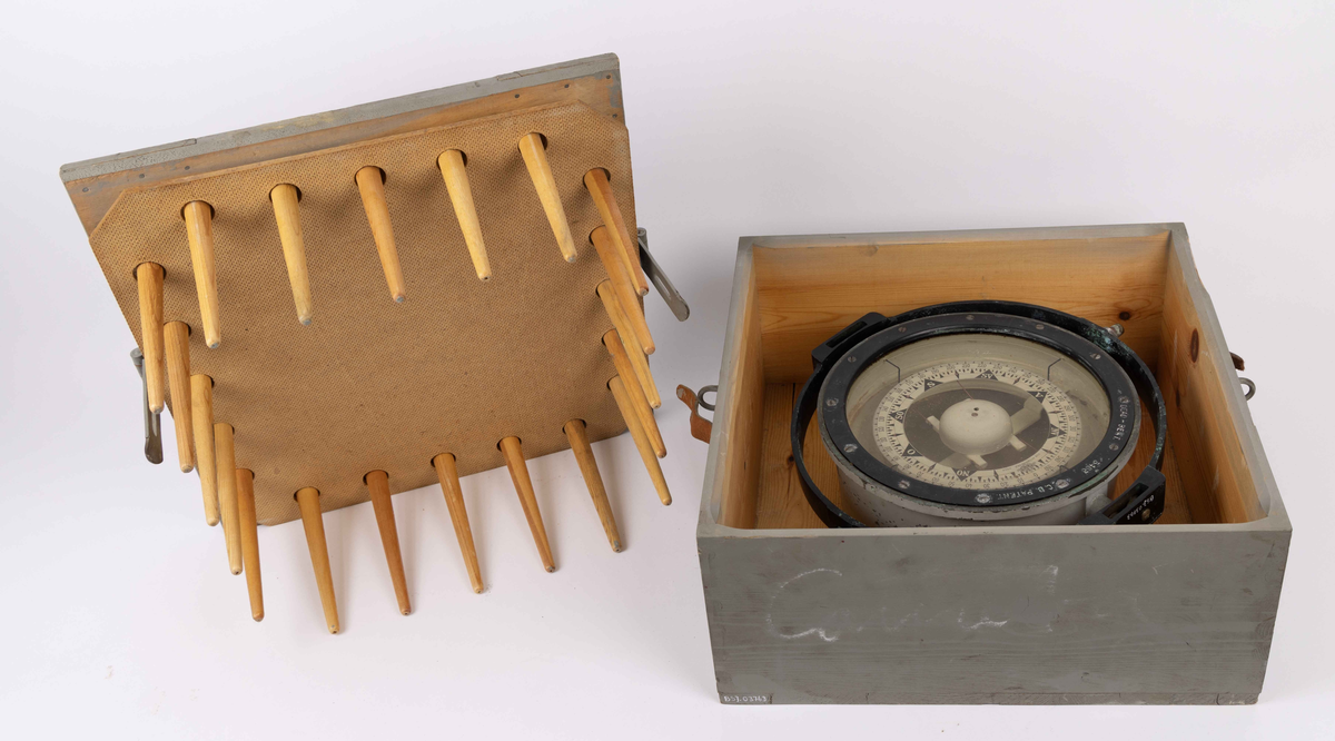 Spritkompass i gråmalt transportkasse av tre. Beregnet til bruk ombord på MS COMETA til BDS. Firkantet transportkasse med løst lokk festet til kasse med hengsel og skinnreim. Lokk med til sammen 20 runde pinner for å holde kompass på plass under transport.