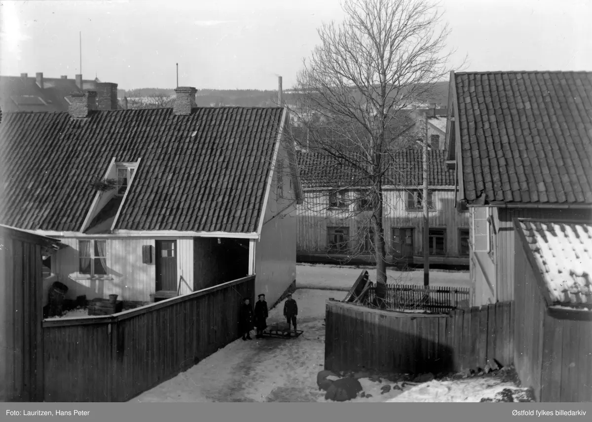 Fotografens egne barn mellom husgjerder i Moss by, ca. 1910-1914.
Fra venstre: Solveig Elvira, Ingertha, Robert William, alle Lauritzen.
Bildet er publisert på s. 162 i boken "Moss som den var".